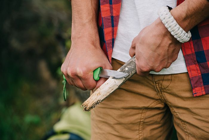 Man with a knife shaving a stick.